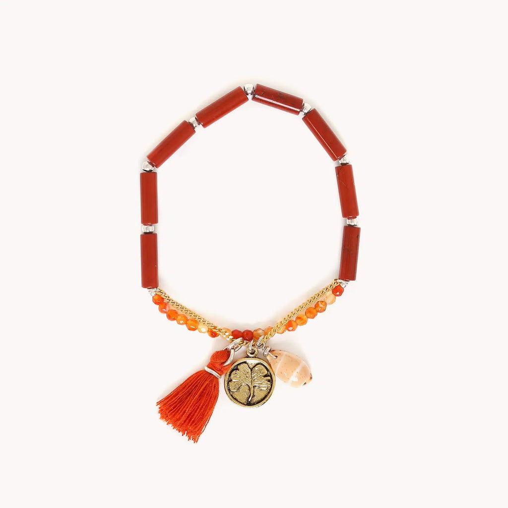 Bracelet extensible composé de perles longues en jaspe rouge, de petites perles rondes facettées en agate rouge et d'une chainette dorée à l'or fin dotée d'une médaille avec un motif feuille de gingko, d'un coquillage et d'un pompon rouge à franges.